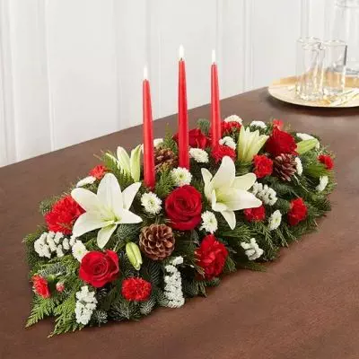 Our traditional table arrangement creates the perfect centerpiece for your Christmas celebration. Beautifully designed with long-lasting blooms in seasonal colors, this fragrant gathering features red taper candles to cast a warm, cozy glow throughout the holidays.